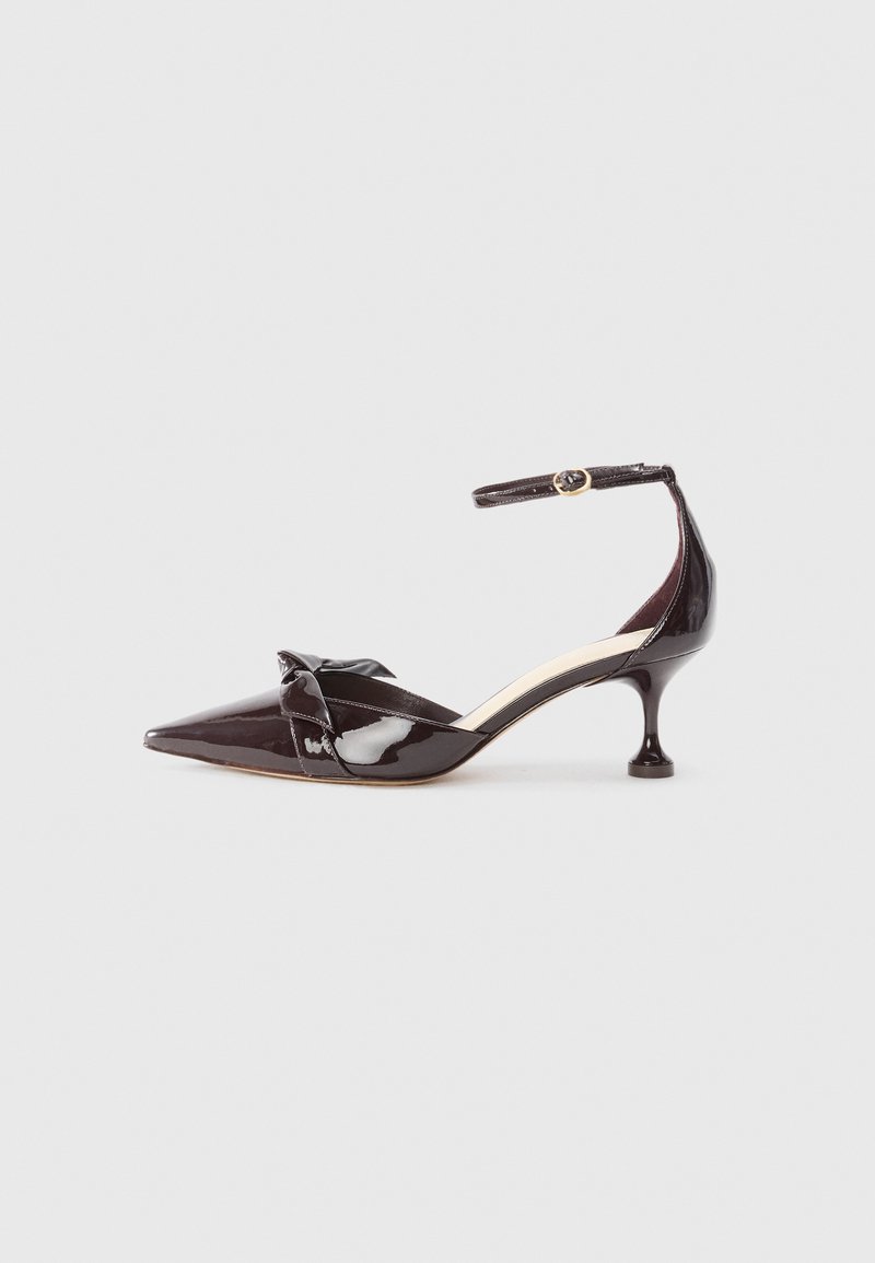 Black patent leather high-heeled shoe with a pointed toe, slender ankle strap, and bow accent at the front, featuring a unique heel design.