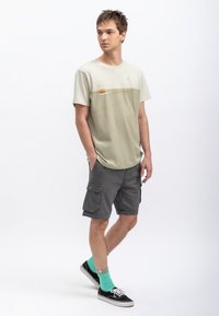 Lichtgroen t-shirt met een horizontaal ontwerp, grijze cargoshorts, teal sokken en zwarte sneakers; casual fit, korte mouwen, minimaal grafisch.
