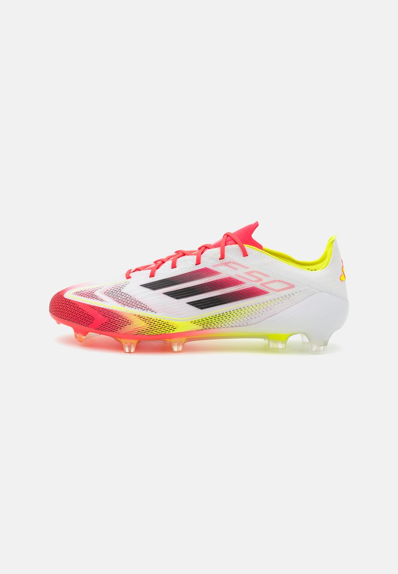 Korki piłkarskie o białej syntetycznej cholewce, intensywnych czerwonych i żółtych akcentach, czarnych paskach oraz przezroczystej podeszwie z sześcioma wkrętami.