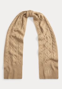 Pletená šála v béžové barvě s copánkovými a diamantovými vzory, měkkou texturou a žebrovanými konci. V rohu je jemně vyšité logo.