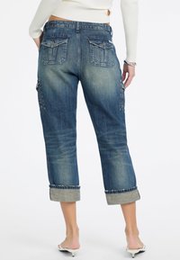 Denim Capri-Hosen in Mittelblau mit leicht verwaschenem Finish, zwei Gesäßtaschen und umgeschlagenen Bündchen mit kontrastierenden Säumen.