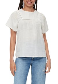 Hvid kortærmet bluse med en afslappet pasform, lavet af et tekstureret stof og med delikat broderi langs halsudskæringen. Kombineret med blå jeans.