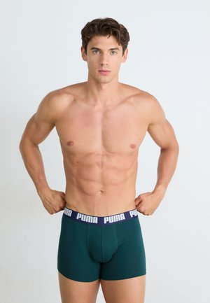 Boxer aderenti verdi in cotone con un cinturino blu navy che presenta il marchio "PUMA" in bianco. Il modello ha un fisico atletico ed è senza maglietta.
