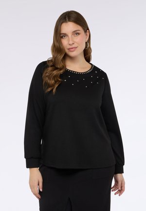 Top nero a maniche lunghe realizzato in tessuto morbido. Presenta un collo rotondo decorato con borchie argento e una leggera puffatura ai polsini delle maniche.