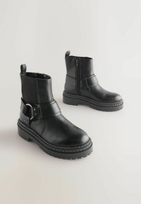 Sorte læder ankelstøvler med sidezipper, spænde detalje og tekstureret gummisål. Har en glat overflade og robust konstruktion.