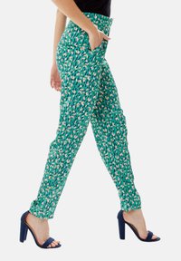 Green patterned trousers with a slim fit, featuring a vibrant pink and black design. Side pockets and ankle-length with elastic waistband.