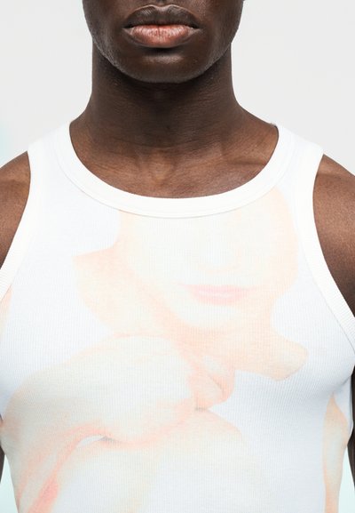 Λευκή αμάνικη μπλούζα με διακριτικό εκτυπωμένο σχέδιο προσώπου, με απαλό ύφασμα και στρογγυλή λαιμόκοψη, ιδανική για καθημερινή χρήση.