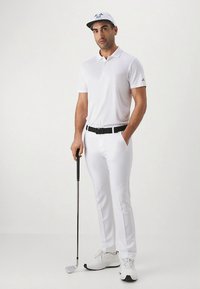 Bílý golfový outfit sestávající z polokošile a upravených kalhot. Nositelný s bílou čepicí se stejným vzorem a logem. Doplňky zahrnují černý pásek a golfovou hůl.