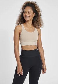 Beige ribbad sport-bh med en bred underdel och tjocka axelband, tillsammans med höga svarta tights med en logo.