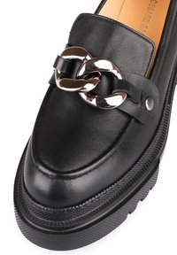 Schwarze Lederloafers mit glänzendem silbernen Kettenakzent, runder Zehenpartie und strukturiertem schwarzen Gummisohle für bessere Bodenhaftung.