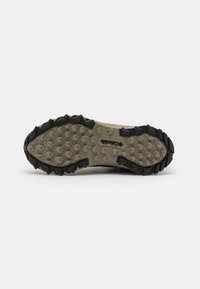 Shoe outsole with a predominantly beige midsole and black rubber traction lugs. Hexagonal and multi-directional tread pattern for grip.