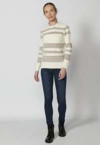 Ribaga kampsun kreemis ja heleses pruunis, tekstureeritud kangas, pikad varrukad, ümar kaelus. Kombineeritud tumesiniste kitsaste teksade ja mustade pahkluupükste kingadega.