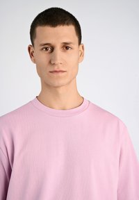 Ljusrosa bomullströja med rund halsringning och mjuk textur. Har en avslappnad passform och minimal design, utan synliga mönster eller accenter.