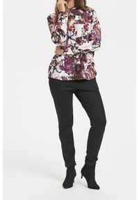 Blusa de manga larga en rosa con estampado floral; pantalones ajustados negros; botas de tacón negro hasta el tobillo; tejido suave con colores vibrantes.