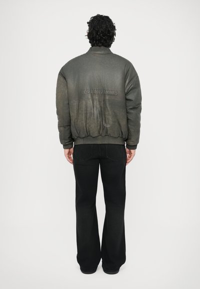 Tamsi, šiek tiek blizgi bombonešio stiliaus striukė su ribinėtu apykakle ir rankogaliais; ant nugaros iškaltas prekinis ženklas; derinama su platėjančiomis juodomis kelnėmis.