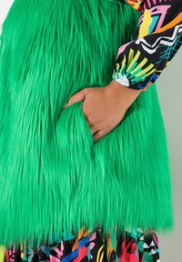 Ljust grön faux fur-plagg med en texturerad finish, som har en dold ficka och en färgglad mönstrad ärm vid manschetten.
