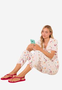 Setti pyjama i lyst stof med farverige frugt- og dyremønstre, prydet med røde accenter. Kombineret med livlige røde flip-flops.