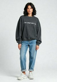 Felpa grigia con testo bianco "HO PARLATO DI TE A CHATGPT", vestibilità oversize, polsini a coste, abbinata a jeans azzurri arrotolati e sneakers bianche.