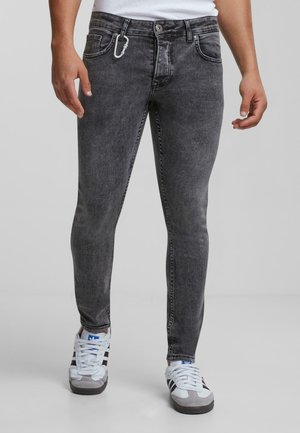 Jeans skinny de denim gris con una textura desgastada, diseño de cinco bolsillos, herrajes plateados y un clip de mosquetón en el lazo del cinturón. Llevados con zapatillas blancas.