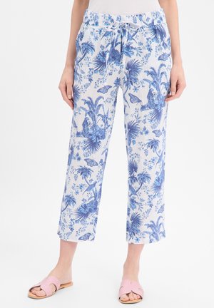 Weiße kurze Hosen mit blauem tropischem Blumen- und Schmetterlingsmuster, elastischem Bund mit Kordelzug, getragen mit pinken Slide-Sandalen.