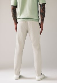 Pantaloni crema leggeri dal taglio dritto, con una consistenza liscia e tasche laterali, abbinati a scarpe da ginnastica bianche.