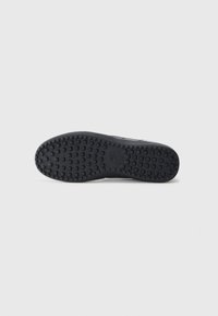 Čierna gumová podrážka topánky so štvorcovým vzorom a logom Nike umiestneným na bielom pozadí.