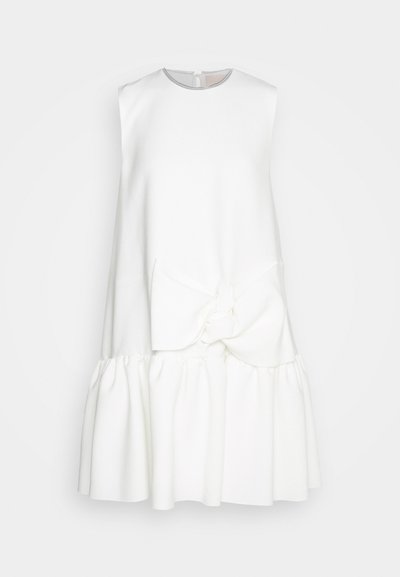 Bjela haljina bez rukava s okruglim izrezom, koja ima istaknutu mašnu na struku i lepršavu, volančastu donju ivicu.