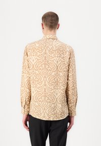 Bež srajca z dolgimi rokavi z teksturiranim damask vzorcem. Ima ovratnik in gumbaste manšete. Tkanina se zdi lahka in fluidna.