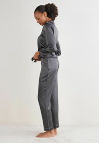 Grijze satijnen lounge-outfit bestaande uit een longsleeve top en broeken met een elastische tailleband. Voorzien van contrasterende stiksels en een relaxte pasvorm.