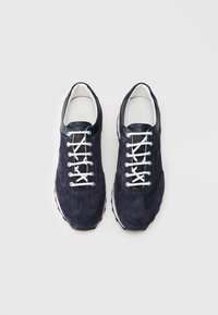 Baskets en suède bleu marine avec des lacets blancs et un talon en cuir contrasté, présentant un design texturé et une semelle en caoutchouc pour l'adhérence.