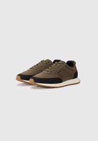Olive green sneakers with black accents, lace-up design, and a textured upper. Features a white midsole and gum rubber outsole.