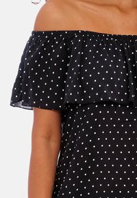 Blusa preta sem mangas com decote rendado, apresentando padrões brancos de diamantes. Feita de tecido leve com acabamentos elásticos.