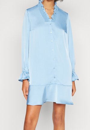 Mujer con vestido de satén azul claro con cuello en V con volantes, cierre frontal con botones, mangas largas con puños con volantes y dobladillo acampanado.