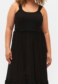 Vestido negro sin mangas con un corsé fruncido, falda acampanada y ribetes con volantes en la cintura y el dobladillo, hecho de tela ligera.