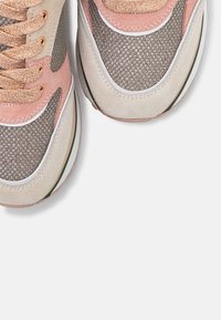 Gros plan de baskets roses, beiges et grises avec un tissu en maille texturé et des empiècements en suède, montrant les zones des orteils et des lacets.