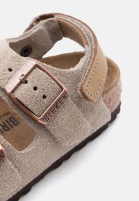Κοντινό πλάνο μπεζ σουέτ σανδαλιού Birkenstock με χαλκόχρυση πόρπη και πά το από φελλό σε λευκό φόντο.