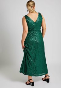 Grön paljettekänning för kvällsevenemang med V-rygg, åtsittande midja och flödande kjol. Har justerbara axelremmar och svarta klacksandaler.