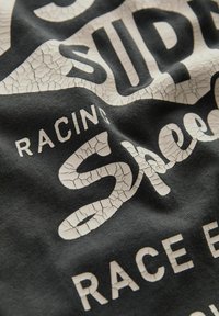 Sort bomulds t-shirt med stort, revnet hvidt tekst som siger "Super" og "Sheep Racing." Blødt, glat stof med et afslappet design.