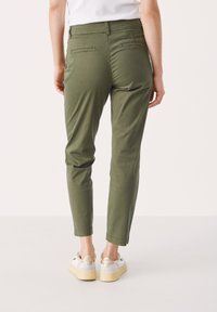 Pantalons fuselés vert olive avec poches arrière, en tissu lisse. Associés à des baskets blanches avec une semelle et des accents beiges.