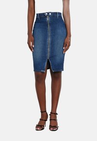 Tamsiai mėlynas džinsinis pieštuko sijonas su priekiniu užtrauktuku, aukštu liemeniu ir plyšiu. Derinamas su juodomis dirželių basutėmis.