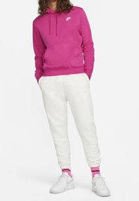 Růžová bavlněná mikina s kapucí a přední kapsou v kombinaci s bílými tepláky. Outfit doplňují bílé tenisky a ponožky s růžovými detaily.