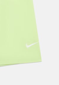 Coin de tissu vert clair avec un petit logo Swoosh Nike blanc près de l'ourlet sur un fond blanc.
