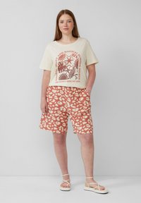 Crème t-shirt met graphic print; roze en witte luipaardprint shorts; relaxte pasvorm; zachte katoen; model draagt minimalistische sandalen met bandjes.