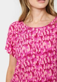 Lyserød T-shirt med korte ærmer, prydet med leopardprint i varierende nuancer af lyserød og magenta. Letvægtsstof med en glat tekstur.