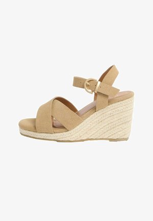 Beige velour kilesandal med krydsede frontstropper, ankelrem, guldfarvet spænde og flettet rebdetalje på hælen.