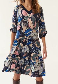 Blumendruckkleid in Marineblau, mit V-Ausschnitt, Dreiviertelärmeln und gestuften Rüschen am Saum. Hergestellt aus leichtem Stoff.