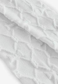 Tessuto a maglia bianca con un motivo testurizzato a forma di diamante e piccoli fiocchi. Texture morbida con dettagli di cucitura visibili.