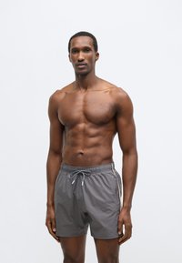 Sive kupaće hlače od lagane tkanine s elastičnim strukom, vezicom i kontrastnim prugastim detaljima sa strane.