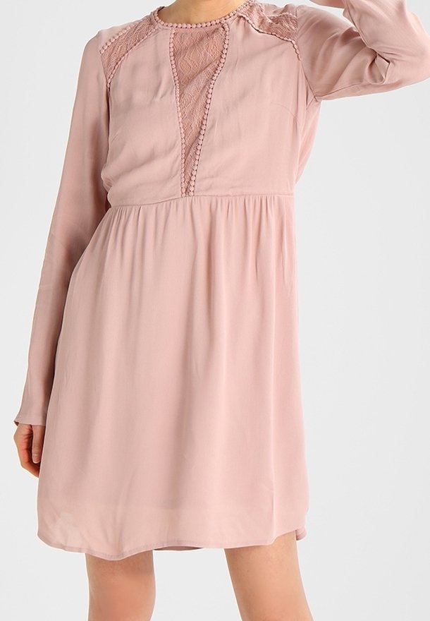 Ljusrosa långärmad klänning med spetsdetaljer vid halsringningen och axlarna, med en lös och flödande silhuett samt texturerade accenter.