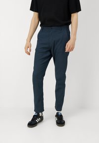 Tmavě modré kalhoty slim fit s texturovanou látkou, standardním páskem a předním zapínáním na knoflík, spárované s černými sportovními botami.